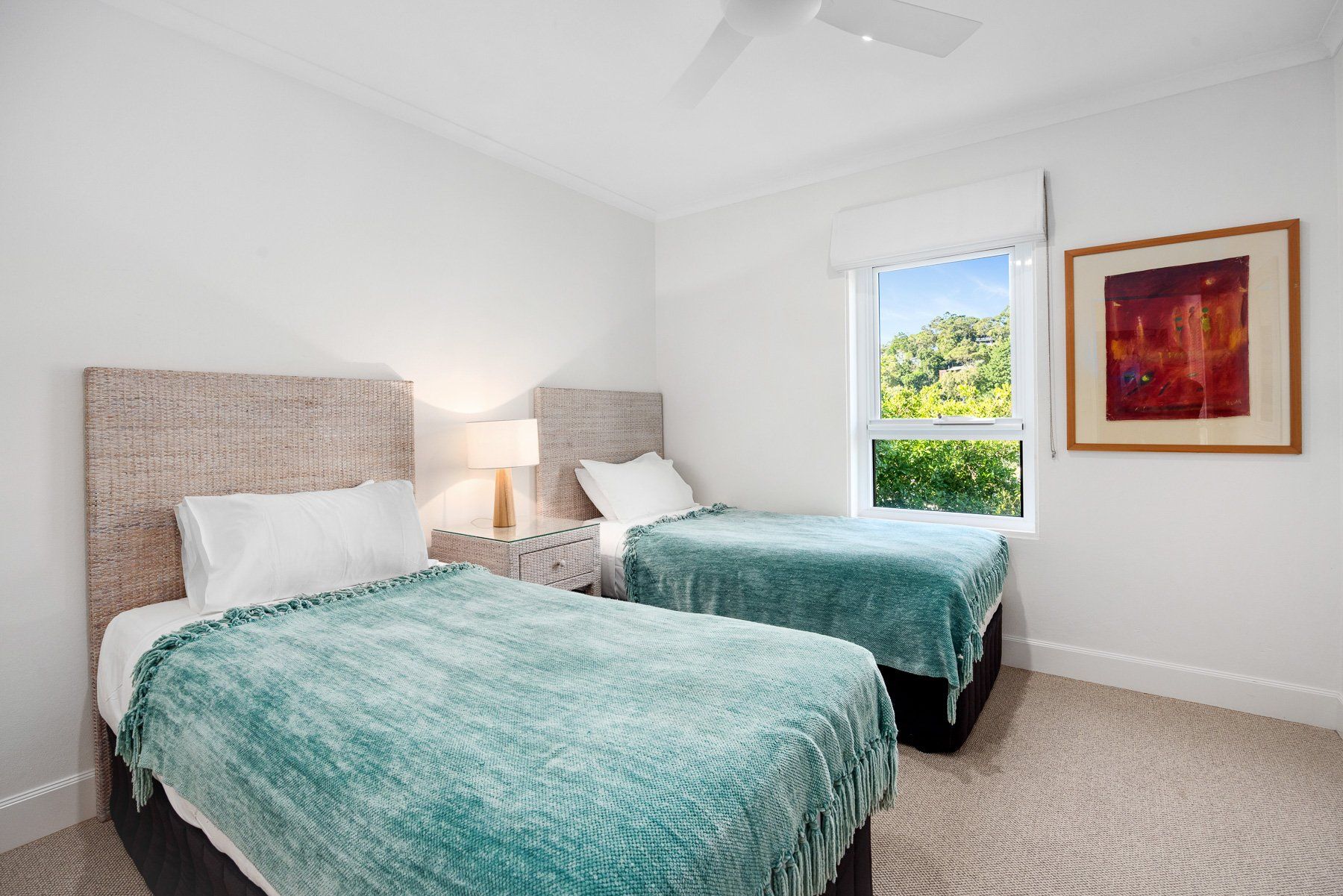 A bedroom with two beds, a nightstand, a lamp, a window with a view, and a framed picture on the wall.