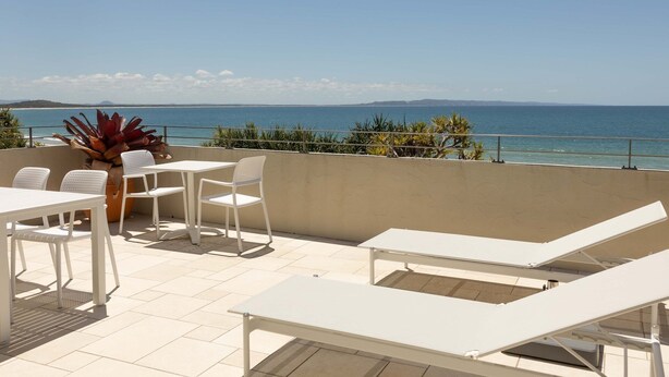 Une terrasse avec des meubles blancs, une plante en pot et une vue sur la mer.