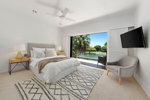 A bedroom with a bed, a nightstand, a TV, a chair, and a view of a pool. - Quay Largo - Riverside Haven (Noosaville)