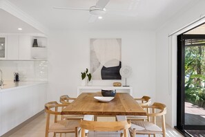A modern kitchen with white cabinetry, a wooden dining table, and chairs. - Quay Largo - Riverside Haven (Noosaville)