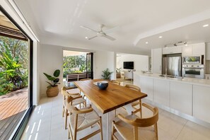 A modern kitchen with a central island, built-in appliances, and a dining area with a wooden table and chairs. - Quay Largo - Riverside Haven (Noosaville)