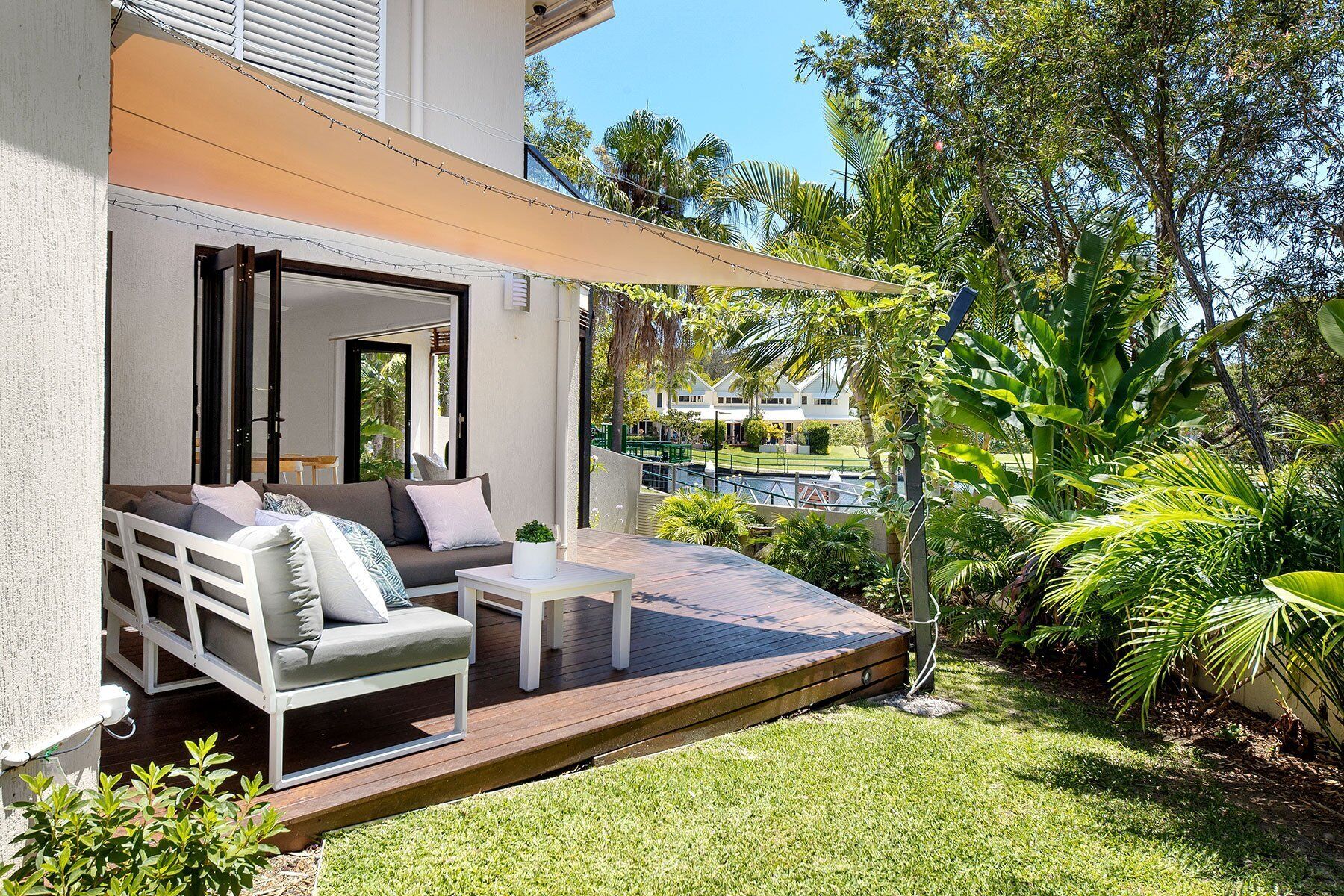 An outdoor seating area with a sofa and table, surrounded by greenery and a pool.