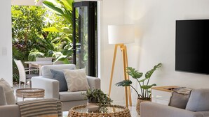 A modern living room with a sofa, coffee table, and floor lamp. There is a large window with a view of greenery outside.