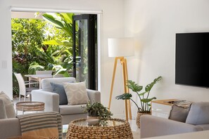 A modern living room with a sofa, coffee table, and floor lamp. There is a large window with a view of greenery outside.