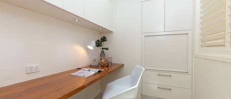 Cocina compacta con muebles blancos, encimera de madera, una silla blanca y una ventana con persianas.
