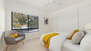 A bedroom with a bed, a chair, a window with blinds, and a ceiling fan.