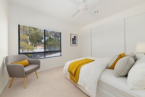 A bedroom with a bed, a chair, a window with blinds, and a ceiling fan.