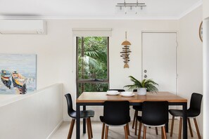 A dining area with a wooden table, black chairs, a potted plant, and a painting of boats on the wall.