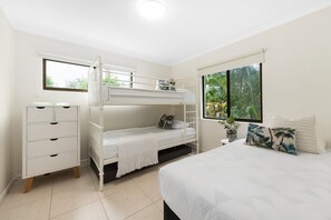 Une chambre avec un lit superposé, un lit simple, une commode et une fenêtre donnant sur un paysage verdoyant.