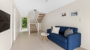 A modern living room with a blue sofa, a small coffee table, a staircase, and a door leading to a balcony. - Soundhaven 1 - Prime Location (Noosa Heads)