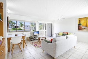 Relax in this spacious living room with a large window offering a view of palm trees and a building outside.