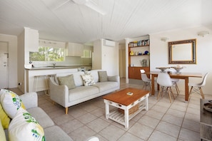 A living room with a sofa, coffee table, and dining area with chairs and a table. - Soundhaven 2 - Steps to Hastings St (Noosa Parade)