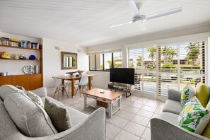 A living room with a TV, sofa, dining table, and chairs. - Soundhaven 2 - Steps to Hastings St (Noosa Parade)