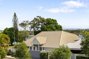 A residential building with a sloped roof, surrounded by lush greenery and a clear sky.