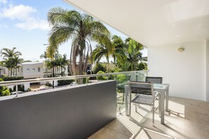 Un balcone con un tavolo e una sedia in vetro, vista su una zona residenziale con palme e case.