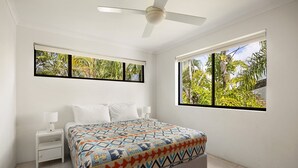 A bedroom with a bed, nightstands, a ceiling fan, and windows with a view of greenery. - Soundhaven 4 - Noosa Parade Value (Noosa Heads)