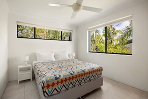 A bedroom with a bed, nightstands, a ceiling fan, and windows with a view of greenery. - Soundhaven 4 - Noosa Parade Value (Noosa Heads)