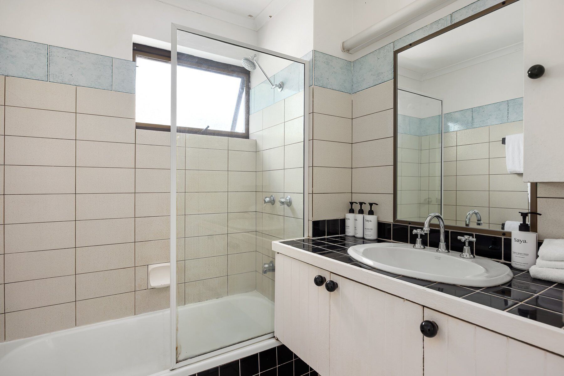 Une salle de bain avec une douche à parois de verre, un lavabo blanc doté d’un plan de travail noir et un grand miroir.