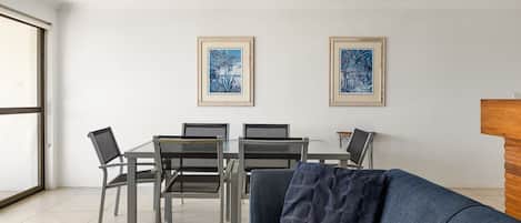 A modern living room with a sofa, a dining table with chairs, and two framed artworks on the wall.