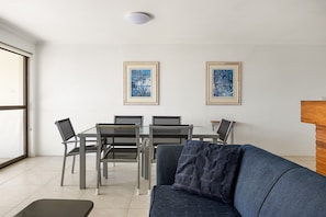 A modern living room with a sofa, a dining table with chairs, and two framed artworks on the wall. - Soundhaven 4 - Noosa Parade Value (Noosa Heads)