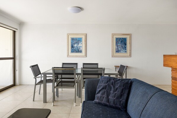 A modern living room with a sofa, a dining table with chairs, and two framed artworks on the wall.