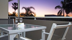 An outdoor dining area with a table and chairs, overlooking palm trees and a sunset. - Soundhaven 4 - Noosa Parade Value (Noosa Heads)