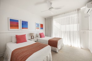 A hotel room with two beds, a ceiling fan, and artwork on the wall.