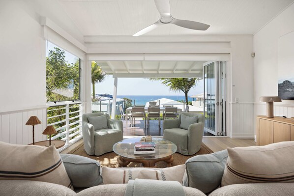 A spacious living area with a view of the ocean, a ceiling fan, and a dining set.