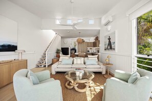A spacious living room with a high ceiling, a staircase, and a view of the outdoors.