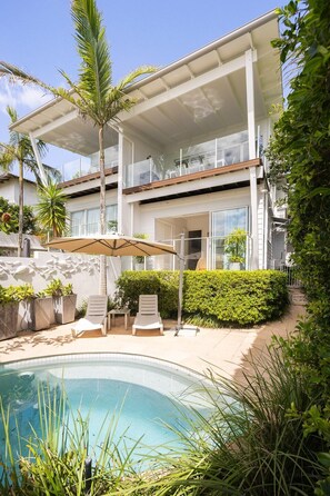 A two-story house with a swimming pool, outdoor seating, and lush greenery.
