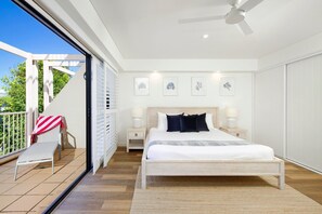 A bedroom with a bed, bedside tables, a ceiling fan, and a view of the outdoors.