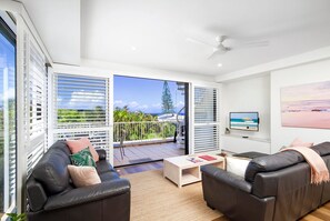 Ein modernes Wohnzimmer mit Sofa, Couchtisch und Fernseher, mit einem Balkon und Meerblick.