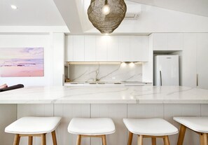 Une cuisine moderne avec des meubles blancs, un plan de travail en marbre et un luminaire suspendu.