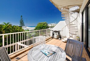 Un balcon avec une table ronde, des chaises, un magazine et un barbecue.
