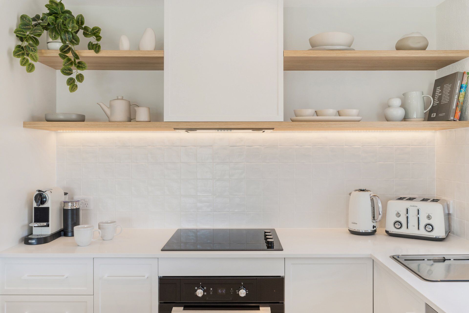 A modern kitchen with white cabinetry, a black induction cooktop, a toaster, and a kettle.