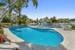 A swimming pool with a curved edge, surrounded by palm trees and lounge chairs.