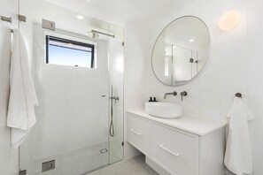 A modern bathroom with a glass shower enclosure, a round mirror, and a white sink.