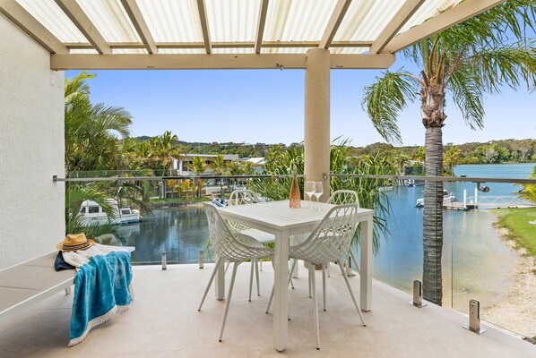 A covered outdoor seating area with a table and chairs, overlooking a body of water and a marina.