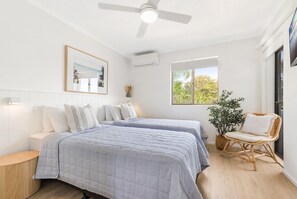 A bedroom with two beds, a ceiling fan, a window with a view, and a chair.
