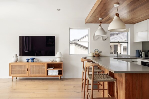 A modern kitchen with a wooden ceiling, a large window, and a flat-screen TV mounted on the wall.