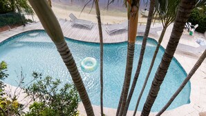 Piscina com deck de madeira, espreguiçadeiras e palmeiras.