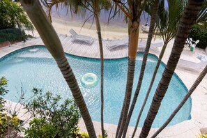 A swimming pool with a wooden deck, lounge chairs, and palm trees.