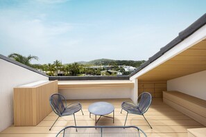 A rooftop terrace with a view of a residential area, two chairs, a small round table, and a wooden bench.