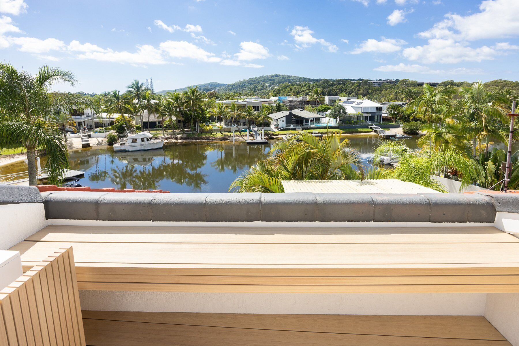 A view of a waterfront property with a pool, boats, and a hillside in the background.