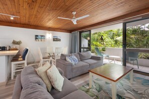 Un salon moderne avec un plafond en bois, un canapé gris, une table basse en bois et un balcon agrémenté de plantes.