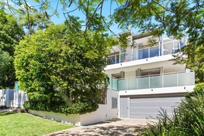 A modern two-story residential building with a balcony, a garage, and lush greenery. - Stunning Duplex with Rooftop Terrace (Little Cove)
