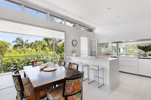 A modern kitchen with a large island, white cabinetry, and a dining area with a wooden table and colorful chairs. - Stunning Duplex with Rooftop Terrace (Little Cove)