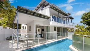 Ett modernt hus i två våningar med en swimmingpool, stora fönster och en balkong.