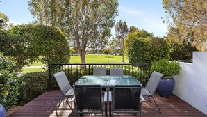 A deck with a glass-top table and four chairs, surrounded by greenery and overlooking a grassy area. - Villa Aqua - Riverside Retreat with Pool (Noosaville)
