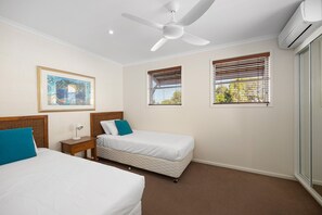 Ein Hotelzimmer mit zwei Betten, einem Deckenventilator, einer Klimaanlage und einem gerahmten Bild an der Wand.